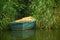Blue wooden boat anchored near the shore among willow foliage