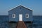 Blue wooden boatshed surrounded by water against clear blue sky