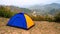 Blue and Yellow tourist camping tent in recreation area among meadow in mountain forest