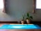Blue yoga mat on wooden floor with plant basket , clock and morning sunlight