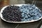 Blueberries and bilberries on the white plate. Ripe bilberries are smaller and darker than blueberries