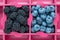 Blueberries and blackberries in a paper box, pink background. Market food product, top view
