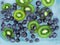 Blueberries and kiwi sinking into blue water with air bubbles