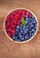 Blueberries and raspberries in clay bowl. Freshly picked berries on rustic background.