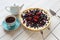 Blueberry open pie on blue plate on bright painted wood with cup of black tea