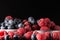 Blueberry and raspberry in white and steel bowls on dark background, close up