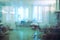 Blurred background in hospital ward with several beds occupied by patients and surrounded by equipment