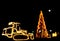 Blurred/bokeh Christmas tree and bulldozer/tractor decorated with lights .