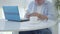 Blurred Caucasian senior man sitting at the table with laptop and counting money. Satisfied mid-adult freelancer with