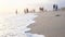 Blurred defocused figures of people on a beach at sunset. White wash of tidal waves on a gray sand at seashore at golden