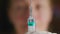 Blurred face of a female doctor, in focus a syringe with a needle and leakage of fluid