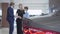 Blurred figures of salesman and two female clients talking in the background of modern car in motor show. Woman choosing