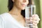 Blurred girl in a white T-shirt holding a glass with water and smiles. Green background