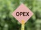 On a blurred green background a pink road sign with the word OPEX - Operational Expenditures