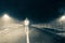 A blurred hooded figure standing in the middle of the road on a winters night, with car headlights lightening up behind him. With