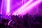 Blurred image of silhouette of raised arms, crowd of people in the front of bright stage lights at concert