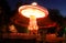 Blurred motion effect around of brightly illuminated rotating high speed carousel merry-go-round. Late in the evening in an