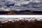 Blurred mountain range under dramatic cloud carpet contrasting with white and blue shimmering salt lake