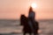 Blurred photo. Woman in summer clothes enjoys riding a horse on a beautiful sandy beach at sunset. Selective focus