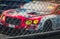 Blurred picture of fence mesh netting and car on racetrack background. Motorsport car racing on asphalt road. Super racing car