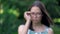 Blurred portrait of asian woman puts up her glasses. Focus appears after putting on glasses. Green trees on the
