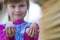 Blurred portrait of cute funny small smiling happy blond girl holding and showing proudly to camera two big clean hen eggs outdoor