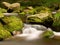 Blurred rapids of autumn mountain river, big mossy boulders obstruct water in foamy motion