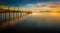 Blurred reflection of the beautiful sunrise in the sky and the pier in the calm blue sea