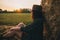 Blurred silhouette of woman sitting at haystack and focus on sunset among trees in summer field