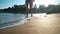 Blurred slim Caucasian young woman walking in sunshine on sandy beach leaving in slow motion. Unrecognizable relaxed