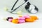 Blurred stethoscope, orange medicine pill, tablets and capsules different colors on white background. Close up colorful pills