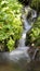 Blurred stream of a mountain stream flowing over moss and stones on the sun