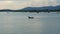 Blurred unidentifiable fisherman with his fishing boat crossing the blue ocean in front of mountains in the background.