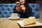Blurred of unknown girl with phone and cup of coffee. Selective focus on the cheesecake