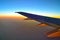 Blurred view of aircraft wing silhouette with  blue sky horizon and clouds background in sun set time, viewed from airplane windo