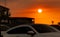 Blurred white Car driving on the road near slum community at sunset with beautiful orange sunset sky. Traffic jam in town while