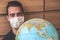 Blurred young man traveller in medical face mask looking at world globe. Coronavirus quarantine. Travel restrictions caused by the