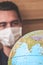 Blurred young man traveller in medical face mask looking at world globe. Coronavirus quarantine. Travel restrictions caused by the