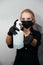 Blurred young woman in black wear and gloves and surgical mask with blue alcohol in her hands in bottle in focus.