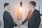 Blurry businesspeople shaking hands together on abstract office interior background with glowing light bulb. Work ideas and
