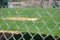 Blurry chain-link fence with a baseball field and buildings on the background under sunlight