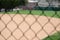 Blurry chain-link fence with a baseball field and buildings on the background under sunlight