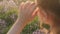 Blurry close-up of young girl hand corrects hairstyle outdoors background field with lavender flowers in evening