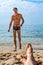 Blurry female legs lie on the sand against the background of a tall handsome wet naked man in swimming trunks emerging from the