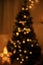 Blurry illuminated christmas tree in eve. Abstract blurred christmas tree with golden lights in evening room. Atmospheric