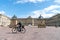 Blurry image of man cycling past large cobblestone courtyayd surrounded by historic building