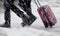 Blurry legs of two people walking fast in heavy snowfall and rolling red suitcase