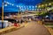 Blurry people hanging out at waterfront boardwalk string lights, beach chairs, patio restaurant dining tables sunset blue hour