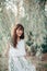 Blurry silhouette of Caucasian woman with long dark brown red hair among willow tree branches leaves outdoors. Casual style real