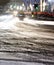 Blurry snowy city street with tire tracks and driving cars light